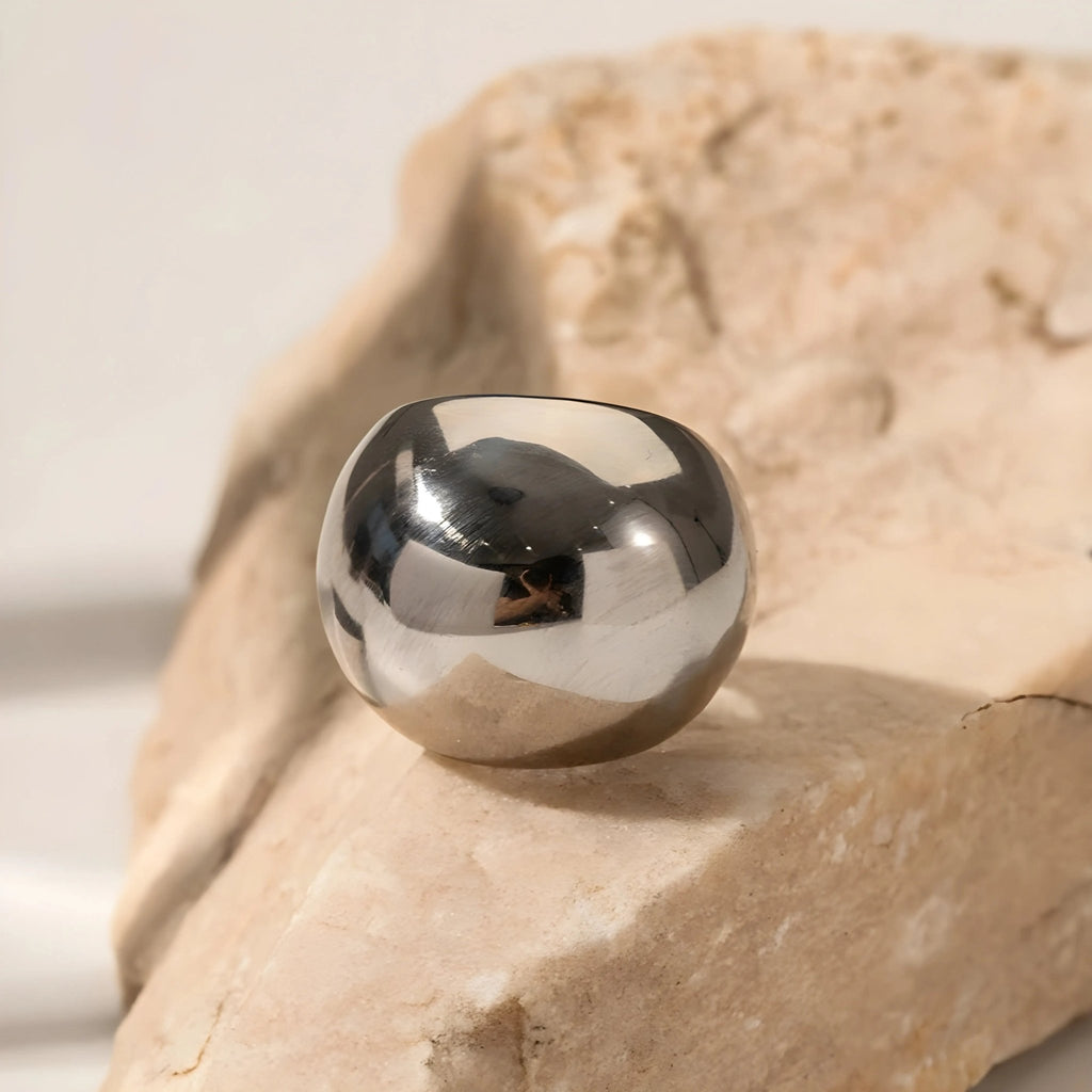 Anello BEHI ERIKAN in acciaio lucido, design scultoreo, su una roccia chiara con riflessi