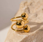 Anello BEHI MIA in acciaio inox placcato oro 18k con tre sfere lucide, gioiello moderno da donna su roccia.