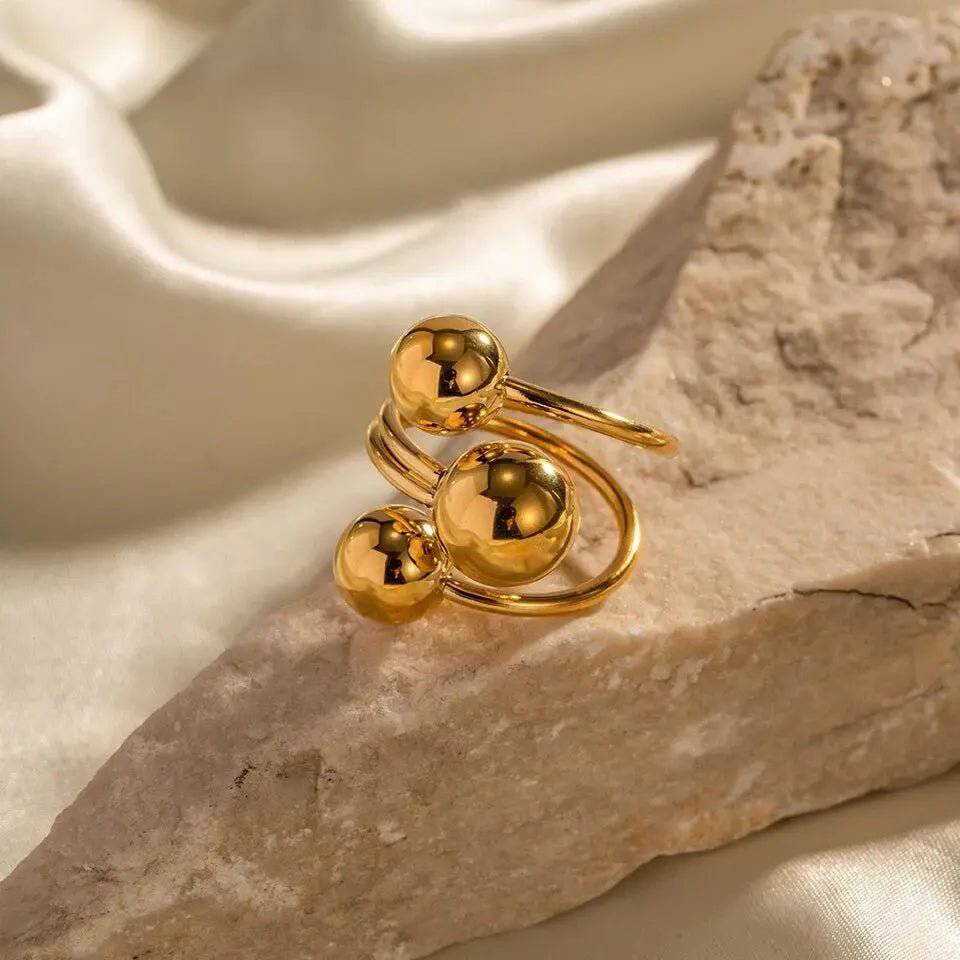 Anello donna BEHI MIA in acciaio dorato 18k con tre sfere lucide su roccia chiara, gioiello moderno.