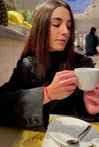 Donna con giacca nera indossa bracciale Filo Rosso con charm Zampa 'My PET' in argento S925 e zirconi, tiene una tazza.