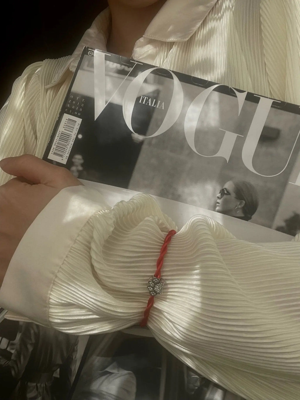Mano con bracciale Filo Rosso del Destino e charm zampa My PET argento S925 con zirconi, tiene rivista Vogue Italia.