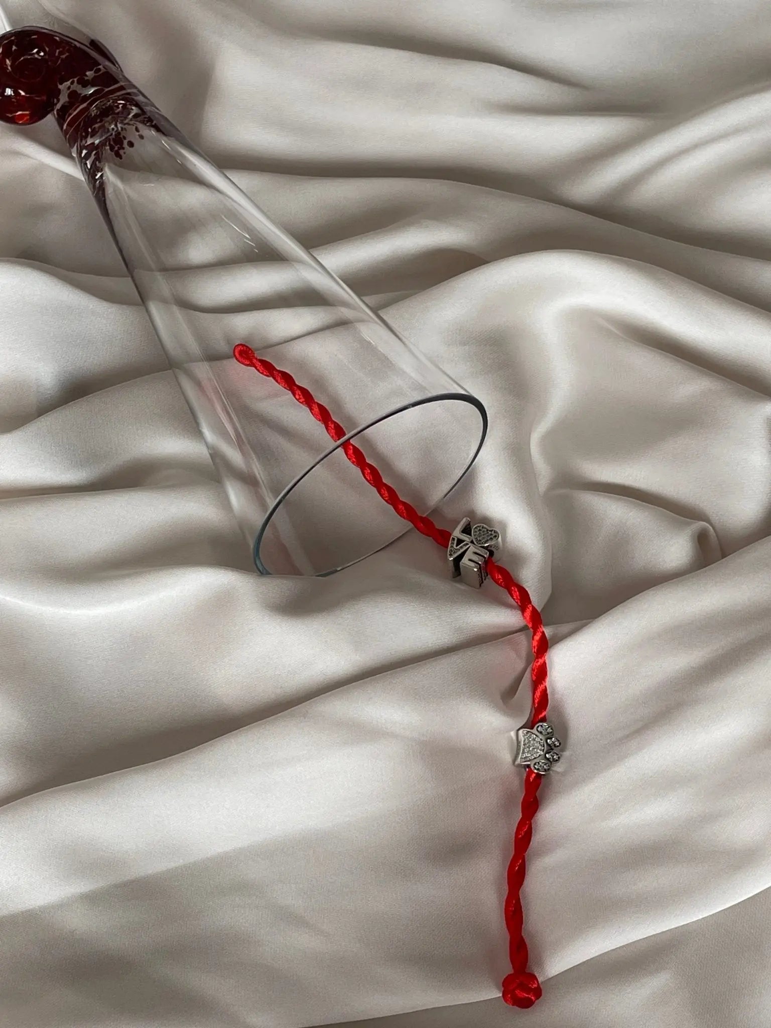 Charm My PET zampa argento S925 con zirconi su Filo Rosso del Destino, vicino a bicchiere su tessuto satinato.