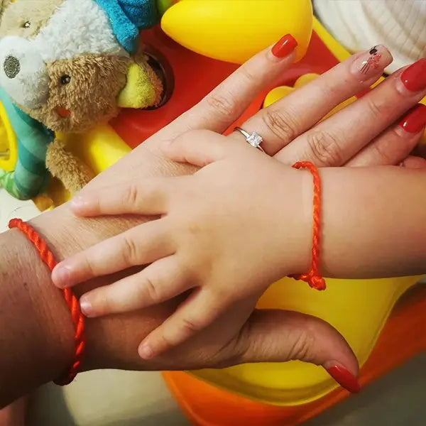 Mani di madre e figlio con bracciali Filo Rosso. Simbolo di legame, protezione e stile raffinato, gioielli artigianali.