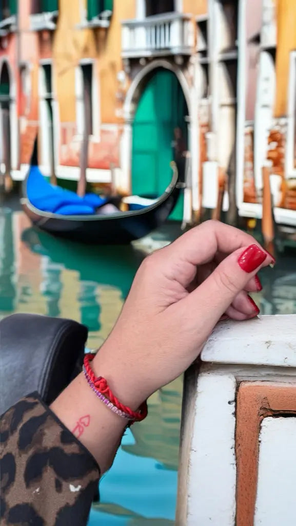 Bracciale Filo Rosso del Destino al polso, gondola sul canale di Venezia, palazzi sullo sfondo. Stile raffinato.