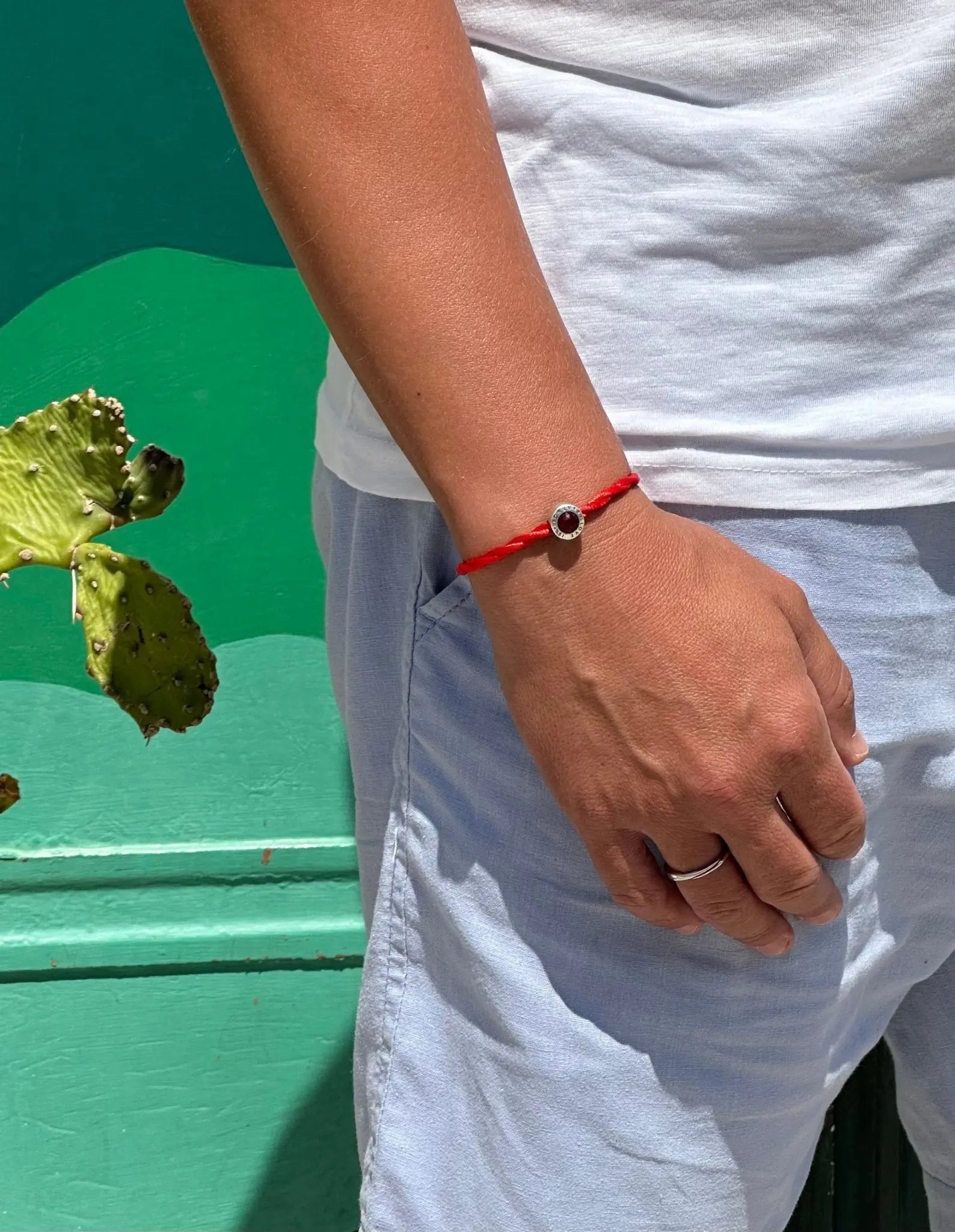 Bracciale Filo Rosso con charm argento S925 "Love is Forever" al polso, sfondo verde vivace, pianta di cactus