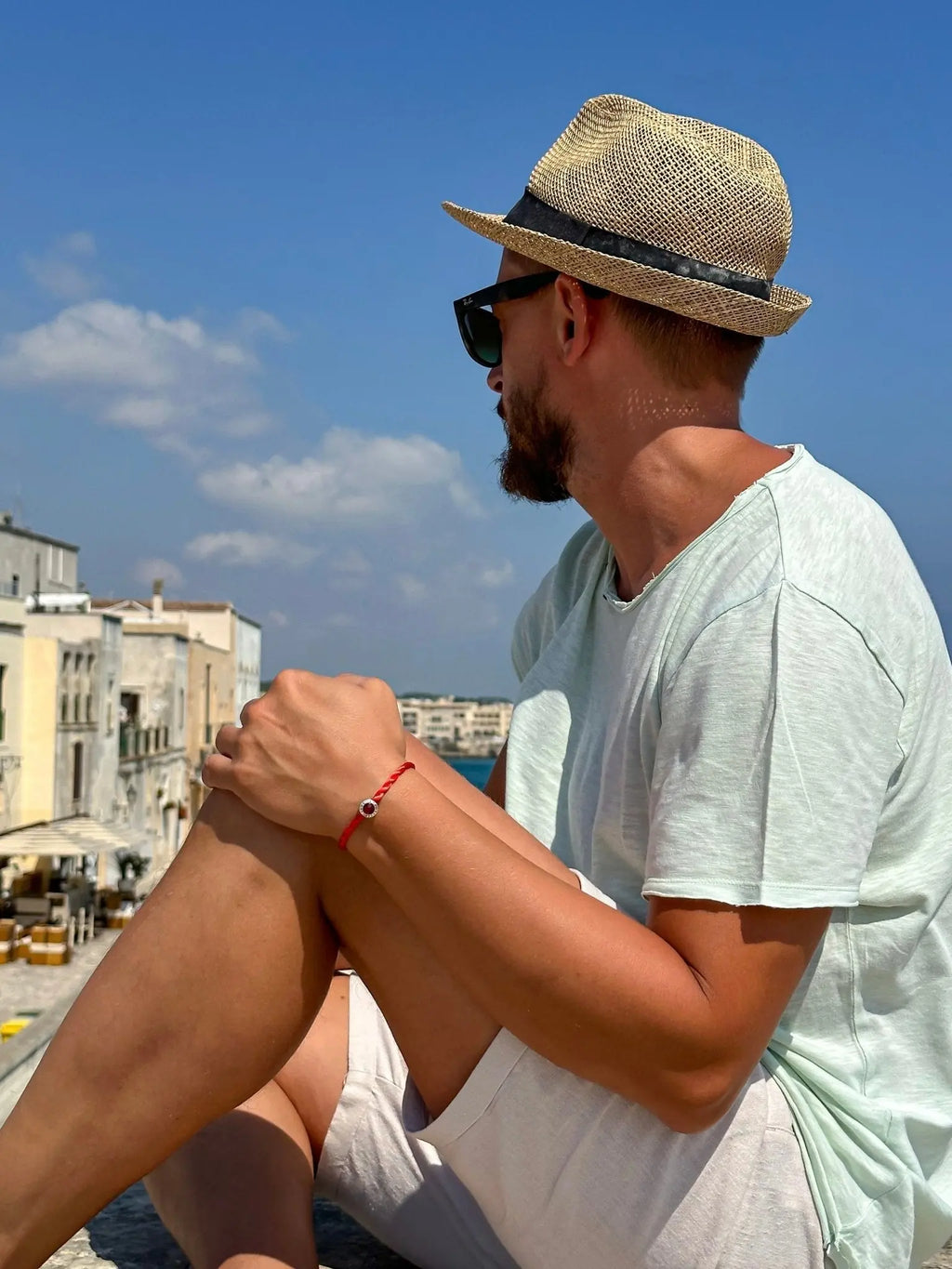 Uomo con cappello di paglia e charm Filo Rosso del Destino "Love is Forever" in argento S925, vista mare