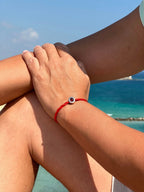 Bracciale filo rosso con charm argento S925 "Love is Forever" su polso, sfondo mare blu.
