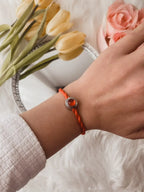 Bracciale filo rosso con charm argento S925 "Love is Forever" al polso, sfondo floreale e specchio