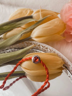 Charm S925 "Love is Forever" con gemma rossa su Filo Rosso del Destino, tra tulipani gialli su vassoio d'argento