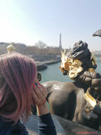 Donna con capelli rosa e bracciale Filo Rosso con Charm Cupido Argento S925, sullo sfondo la Torre Eiffel