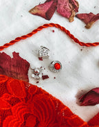 Charm Renna Rudolph in argento S925, charm casa famiglia e charm rosso Filo Rosso su tessuto bianco con petali.